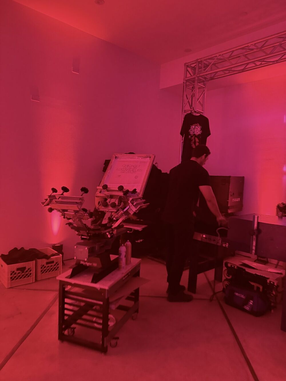 A multi-color screen-printing press set up under event truss with a finished printed tee hanging on display